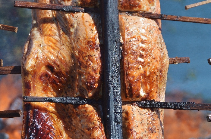 salmon baking over open fire pit on skewers